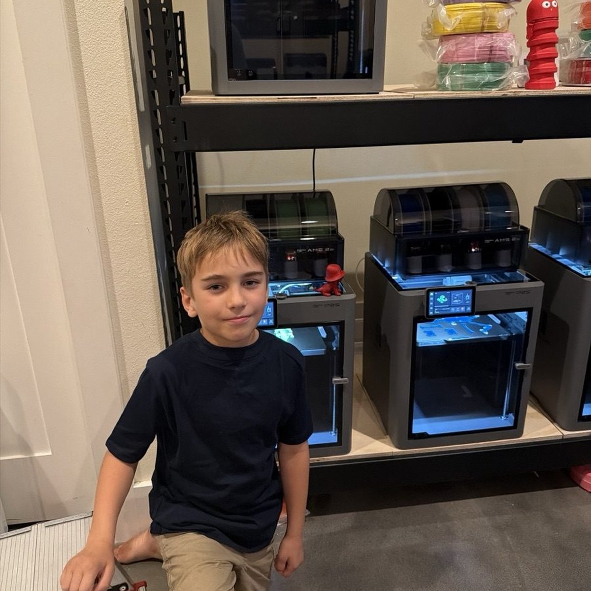 Joseph sitting in front of a row of Bambu Lab P2S printers, one with a small printed octopus on top