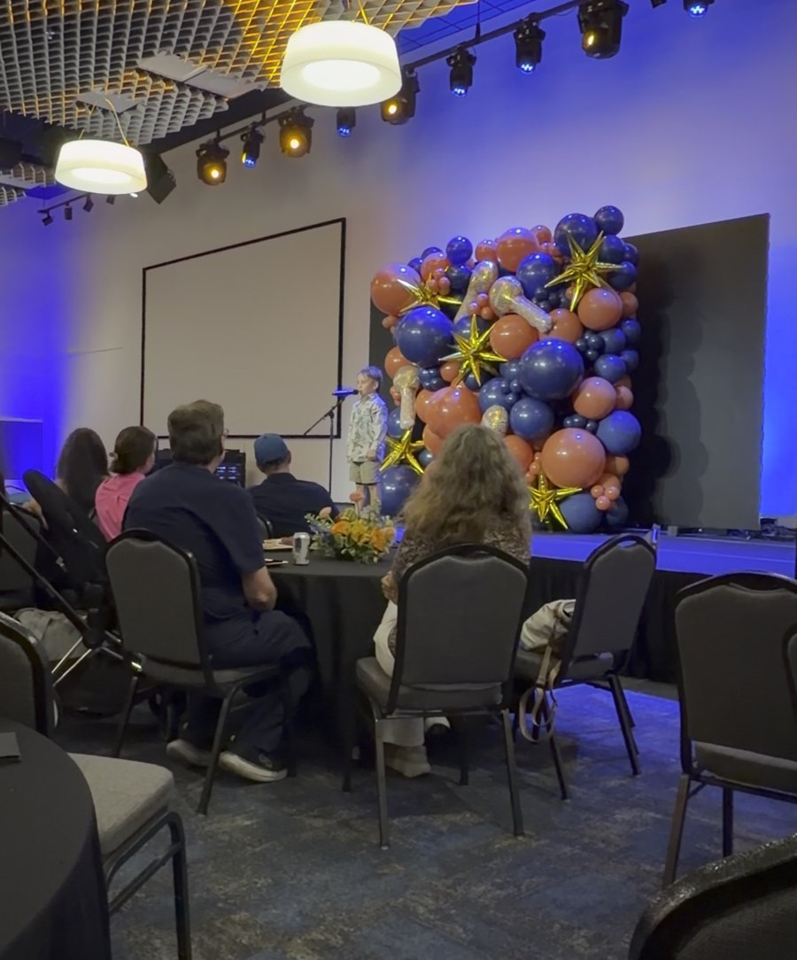 Joseph on stage giving a talk in front of a balloon backdrop
