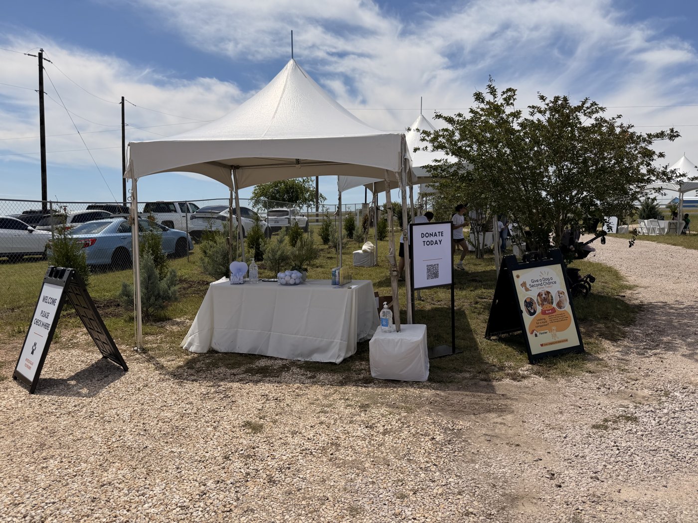 The welcome tent at Living Grace Canine Ranch in Bertram, Texas, with a donation stand and foster-a-dog signs